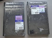 Photo showing two packs of Blueline account books still sealed in original shrink-wrap packaging, label visible with product details.