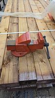 Cast iron bench vise painted red, positioned on wooden surface, showing side profile and jaw mechanism.