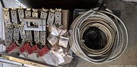 Photo showing multiple used electrical outlets including standard and red outlets, a double outlet wall plate, unopened bags of connectors, and metal flexible wires coiled on the right.