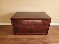 Front view of the dark wood handmade chest showing smooth finish and decorative metal emblem in center