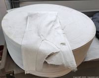 Large roll of white Anmolfabtex fabric with a sample piece laid across the top showing texture and color.