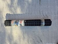 Rolled black floor mat with textured nodules surface and interlocking edges, photographed on concrete floor.