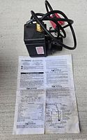 Photo of Little Giant PE-2YSA pump resting on instruction manual, showing pump body and attached electrical cord.