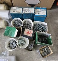 Multiple boxes and containers of industrial rivets, bolts, nuts, washers, and other hardware displayed grouped together on a floor.
