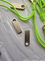 Close-up photo of two metallic USB flash drives with neon green lanyards on a clear plastic surface. One USB shows the engraved brand 'Yjazzen'.