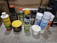 Photo showing front view of machinery maintenance products, including bottles and spray cans placed on a floor with a cardboard box background.