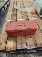 Closed red metal toolbox on wooden surface with visible wear and handle on lid