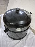 Black charcoal grill/smoker showing dome-shaped lid with thermometer and vent