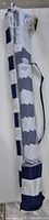 Beach umbrella in its mesh carry bag with a white and blue striped pattern visible under the mesh. The bag has a strap and the umbrella is folded inside.