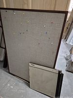 Large fabric covered pin board with multiple colored push pins, wooden frame visible, standing upright.