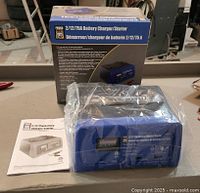 Photo of the Powerfist 2/12/75A Battery Charger/Starter unit sealed in plastic, with original box and user manual on the side.