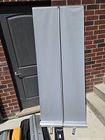 Photo of a rolled-up aluminum roll-up sign banner about 7 feet tall next to a door.