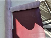 Large roll of maroon Enduratex vinyl partially unrolled showing the texture and color.