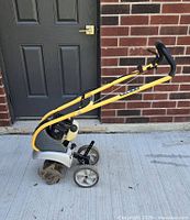 Side view showing yellow handles, engine housing, rear wheels, and tines partially visible on front.