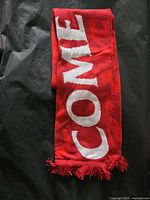 Photo of folded Toronto FC red scarf showing white letters spelling 'COME' and fringe ends.