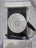 Top view of USB turntable with clear dust cover, software installation CD on platter, power cable visible, and white foam packaging ends.