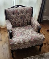 Full view of the vintage floral upholstered armchair with solid wood frame positioned on a wooden floor near a window.