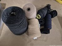 Photo of three yarn spools in shades of black and beige along with six rolled black Velcro strips placed on a beige surface.