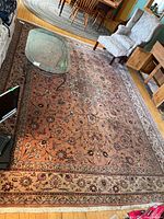Full view of hand-knotted rug on wooden floor with glass coffee table and sofa