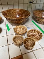 Photo showing the large Rockingham Bennington serving bowl alongside four smaller matching bowls with mottled brown and yellow glaze, all placed on a tiled countertop.