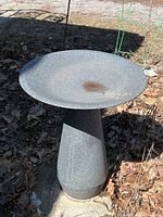 Front view of grey speckled plastic bird bath on concrete slab