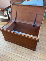 Open wooden blanket box showing the interior and metal hinges holding the lid.