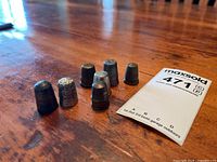 Overview of all seven metal thimbles arranged on wooden surface alongside lot card