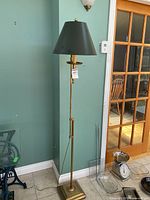 Full view of tall brass floor lamp with green shade, showing entire lamp and cord on tile floor.