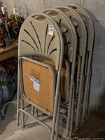 Side angle view of four beige folding card table chairs stacked showing curved backs with fan pattern and upholstered seats.