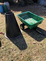 Green plastic John Deere garden wagon with hitch bar next to tall black plastic cone on grass