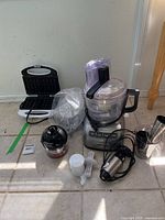 Full view of KitchenAid food processor, waffle maker, Cuisinart Smart Stick hand blender with accessories on tile floor.