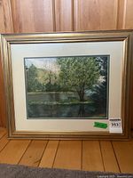 Full frontal photo of the framed watercolour painting showing the lake scene with the tree and picnic bench, including mat and gold frame.
