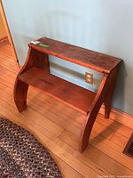 Front angle view of the two-step pine stool showing its curved supports and worn surface.