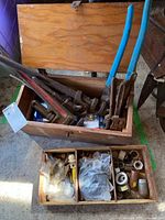 Wooden toolbox open showing five pipe wrenches inside and removable trays below with plumbing hardware.