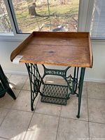 Full view of the repurposed Singer treadle sewing machine base with pine table top, showing the wooden surface and full iron base.