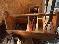 Wooden tool caddy with various hand tools inside, placed on a wooden surface.