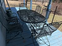 Front angle view of oval metal mesh table with six matching chairs on porch