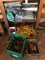 Multiple tarps folded and stacked on shelf, along with coiled yellow rope and bins with straps.
