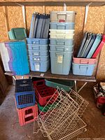 Stack and arrangement of plastic totes, milk crates, and wire baskets on and below a wooden shelf.