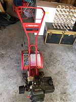 Front-facing overview of entire rototiller showing handle, engine, tines and wheels
