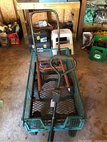 Green metal utility wagon with a mesh bottom and sides, shown from the top with handle visible along with the dolly inside the wagon.
