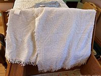 Full view of white vintage chenille bedspread draped over a piece of furniture showing hobnail texture and fringed edge.