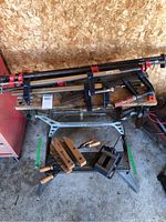 Wide view of portable Work Mate workbench with assortment of clamps on and around it including F-clamps and wooden hand screw clamps.