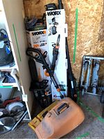 Multiple WORX 20V PowerShare tool boxes and assembled tools leaning against wall with Stihl scabbard on floor