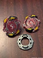Two red transparent energy layers with black and yellow accents and a metal ring component on a wooden surface