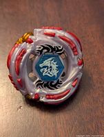 Top view of Beyblade Metal Fight Meteo L-Drago showing the detailed gray and red plastic design with a blue center featuring a white dragon emblem.