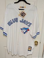 Full view of jersey hanging on a black hanger showing Blue Jays lettering and team logo with Cooperstown Collection tag.