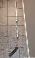 Full view of white hockey stick with 'VICTORIAVILLE' text on shaft, yellow-black design near the taped blade, showing wear.