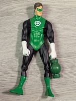 Single articulated green lantern action figure with lantern accessory on a gray wooden floor background