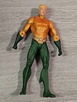 Front standing view of the Aquaman figure showing detailed orange scaled armor and green gloves and pants.